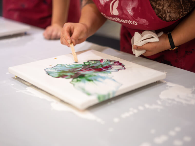 Person wearing apron pouring paint at a fluid art class.